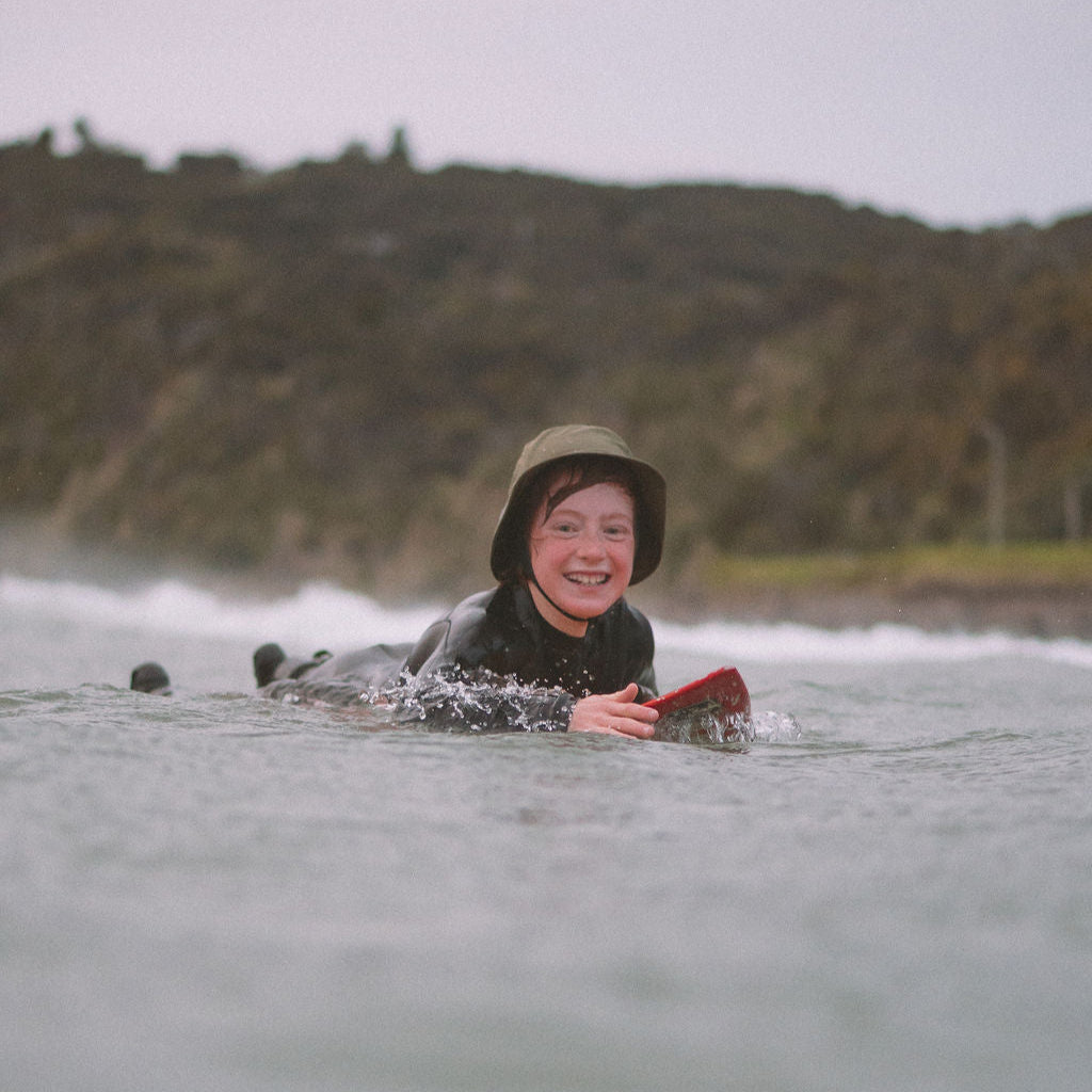A child surfer paddling out with surfshell on to protect his head