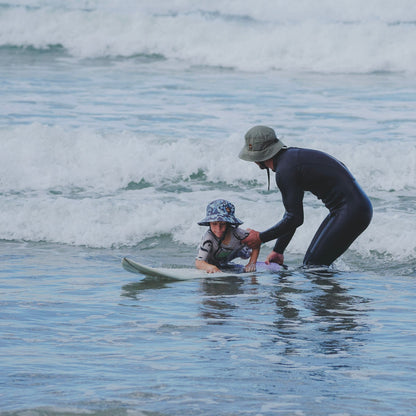 A father and son in the water learning to surf wearing surfshell protective surf hats
